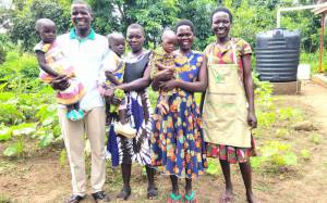 From left, Okello Innocent and Nancy, each carrying one of their twins, pose for a photo with members of the Nutrition Model Home in Kole District.
